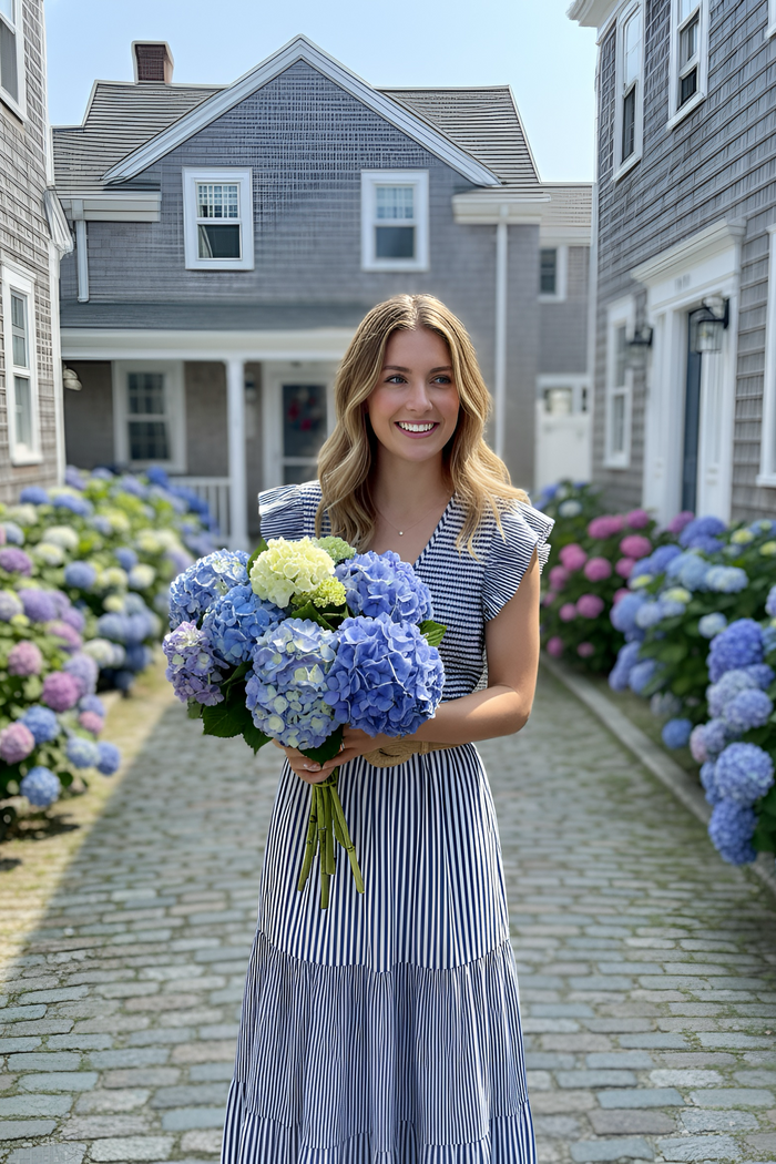 Woman holding flowers in a picturesque street with hydrangeas.