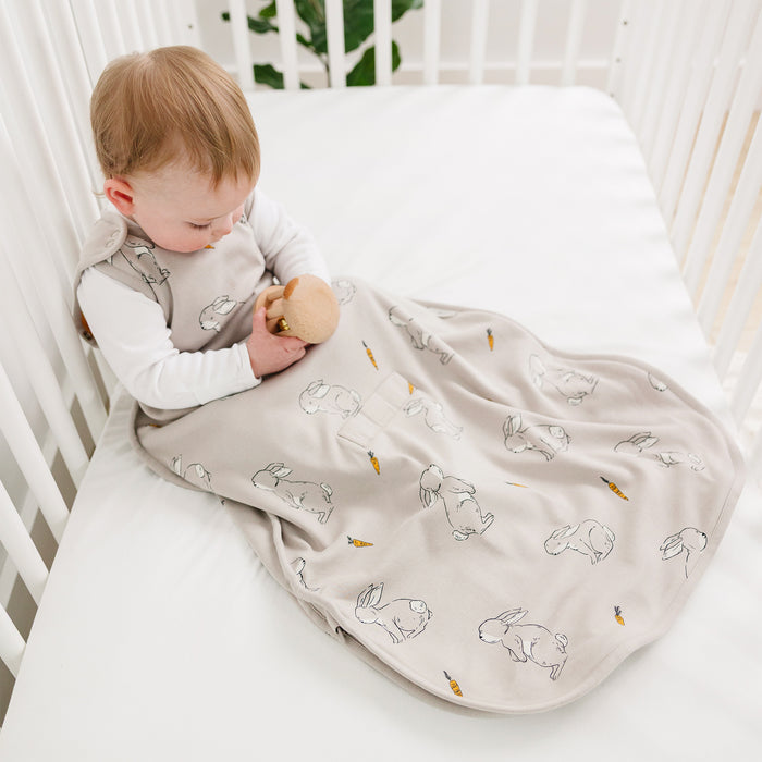 Child in a crib with a beige waddle blanket featuring bunny patterns.
