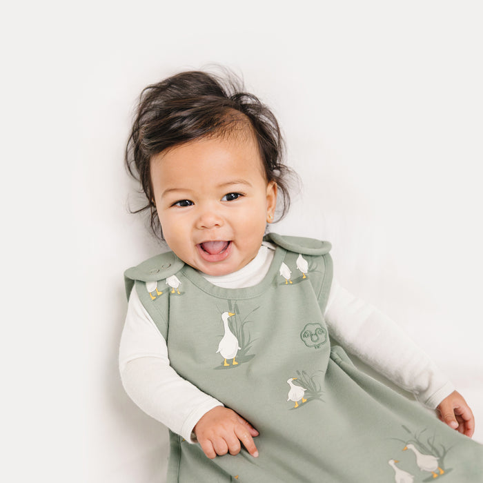 Baby wearing a green sleep sack with duck patterns on a white background