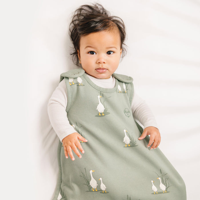Baby wearing a green sleep sack with duck designs on a white background