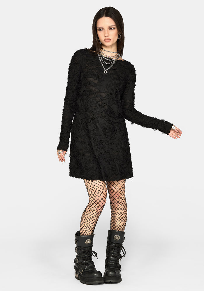 A model wearing a black long-sleeve textured mini dress, black fishnet tights, and black combat boots, standing against a light gray studio background.