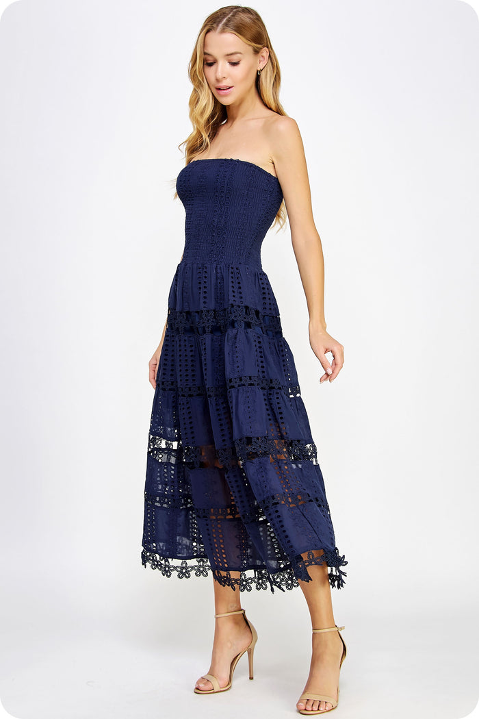 Woman wearing a navy strapless dress with lace details on a white background