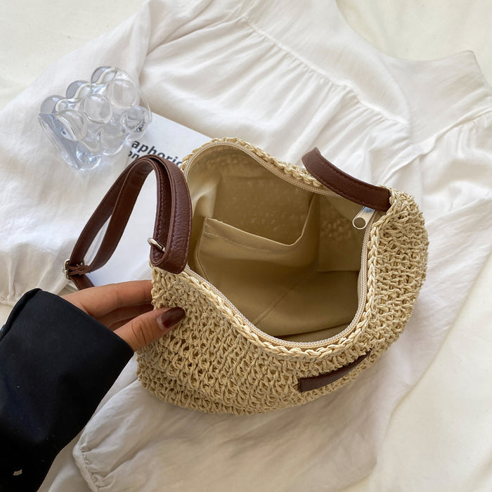 Hand holding a woven handbag with brown handles on a light background