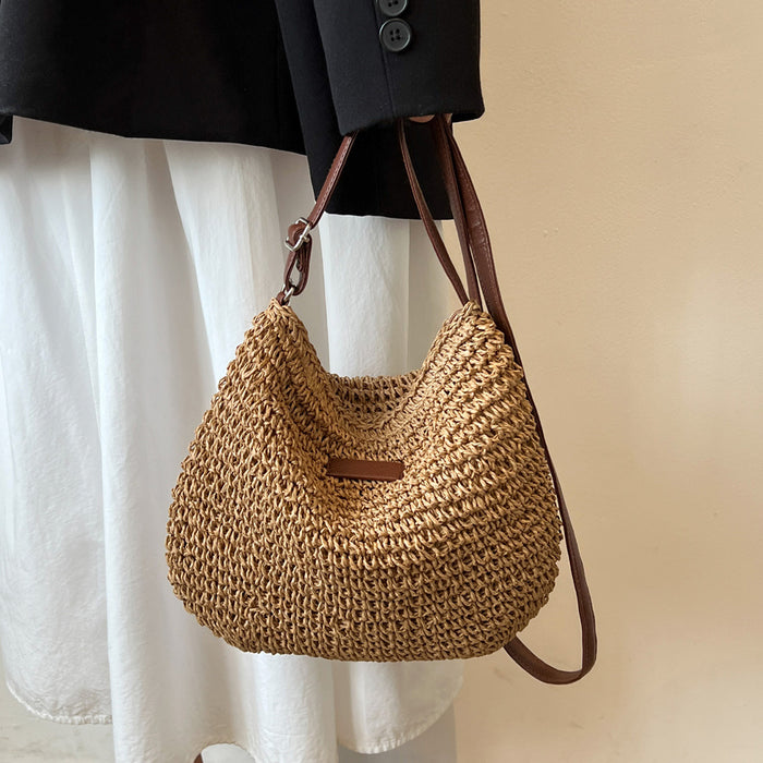 Woven handbag with leather strap held by a person wearing a black coat and white pants.