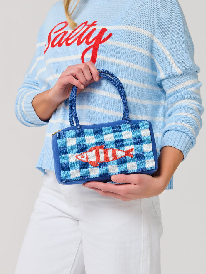 Person holding a blue checkered handbag with an orange fish design, wearing a light blue sweater with 'Salty' text.
