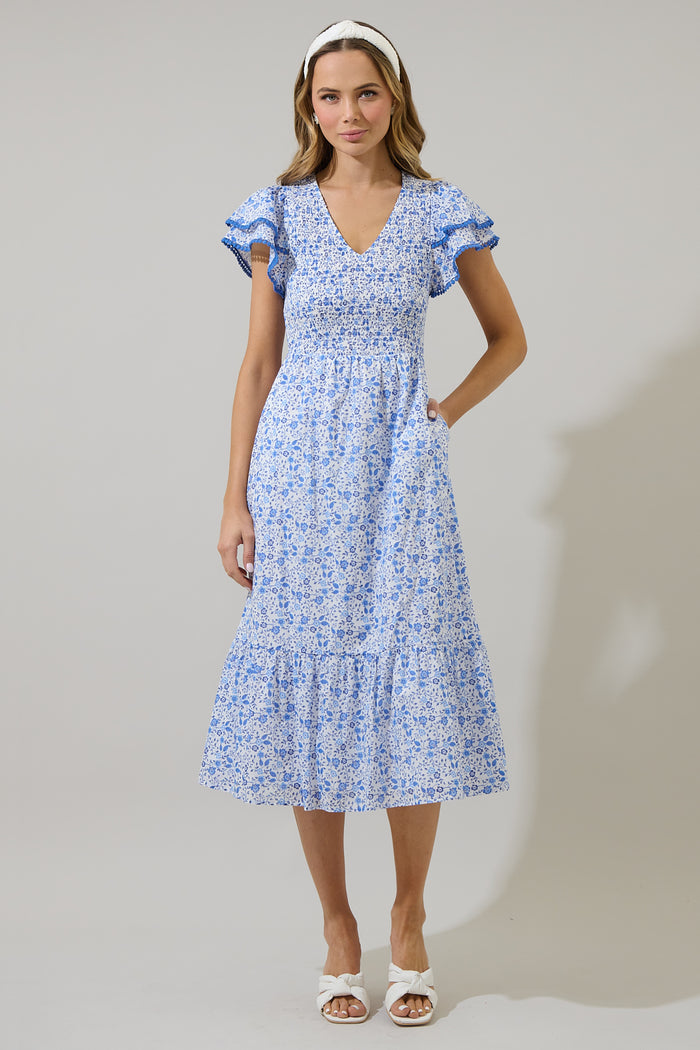 Woman wearing a blue and white floral dress with ruffled sleeves and blue trim against a white background