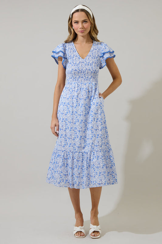 Woman wearing a blue and white floral dress with ruffled sleeves and blue trim against a white background