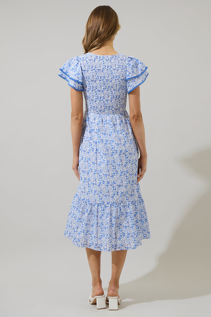 Woman wearing a blue and white floral dress with ruffled sleeves and blue trim against a white background