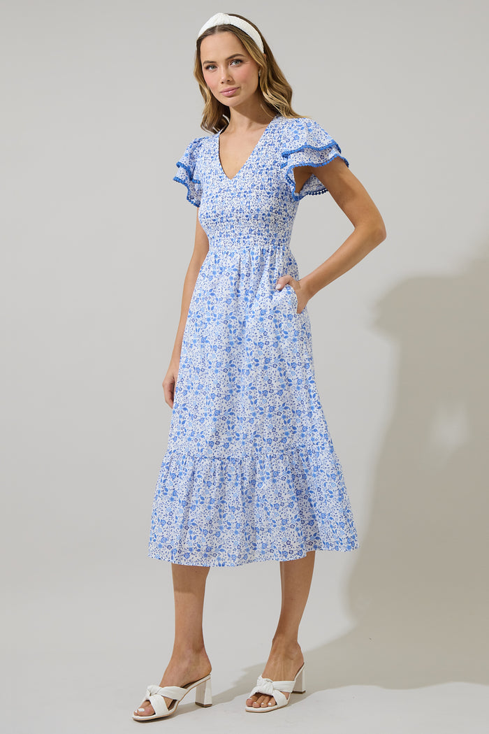 Woman wearing a blue and white floral dress with ruffled sleeves and blue trim against a white background