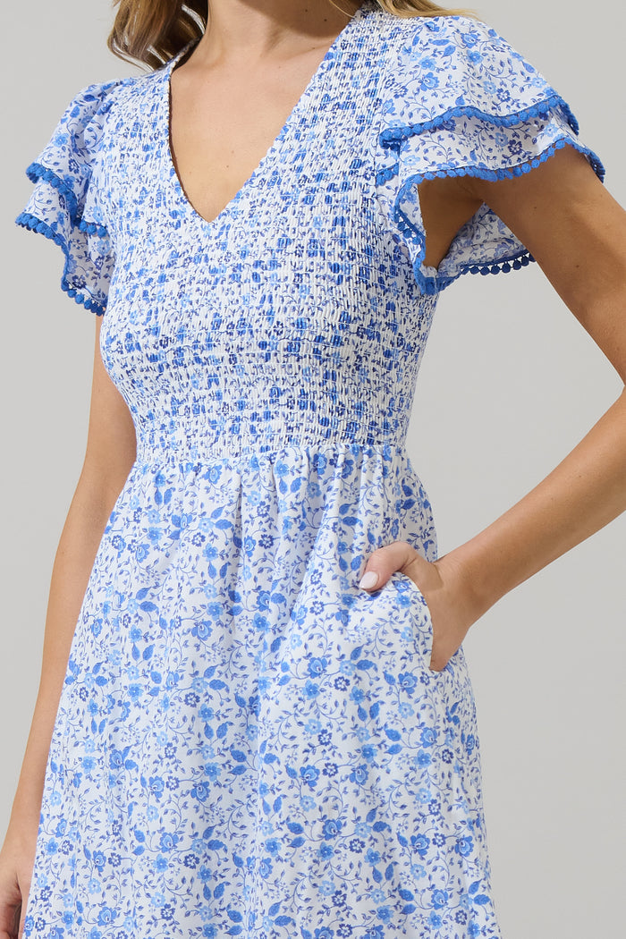 Woman wearing a blue and white floral dress with ruffled sleeves and blue trim against a white background