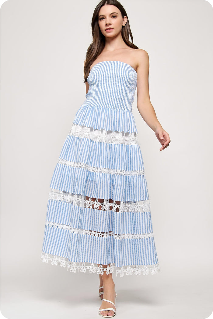 Woman wearing a blue and white strapless striped dress with lace details on a white background