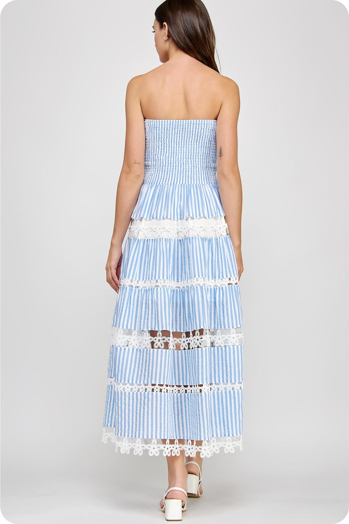 Woman wearing a blue and white strapless striped dress with lace details on a white background