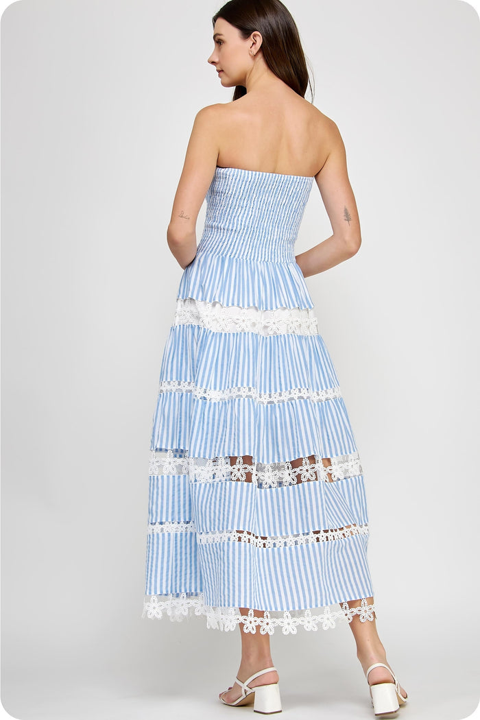Woman wearing a blue and white strapless striped dress with lace details on a white background