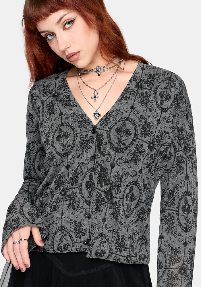 Woman wearing a black patterned v-neckline cardigan over a black outfit on a white background