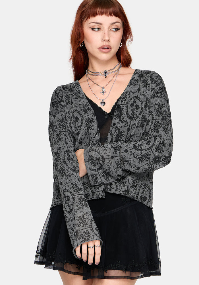 Woman wearing a black patterned cardigan over a black top and skirt on a white background