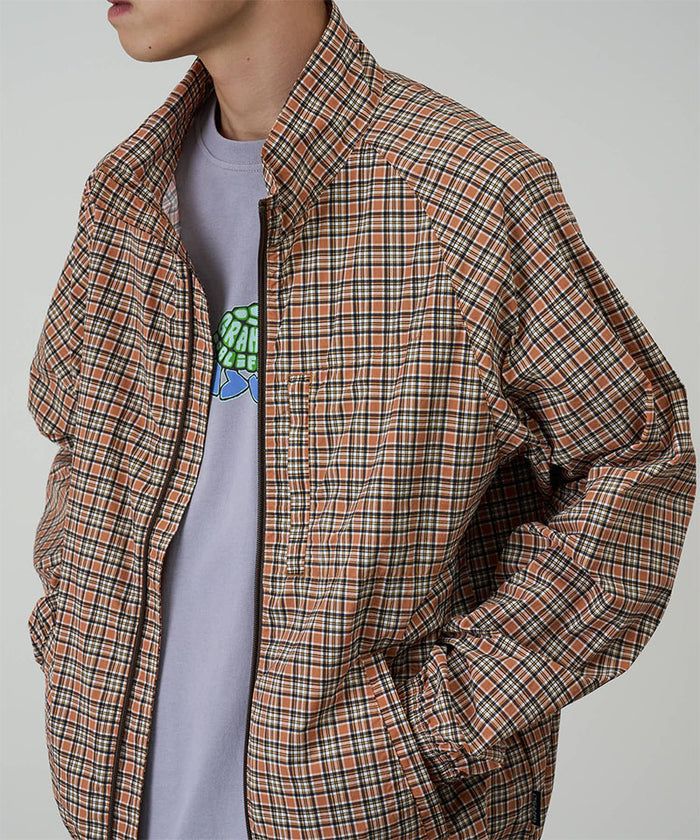 Model wearing a Gramicci brick colored Checkered Shell Jacket against a light-tone background.