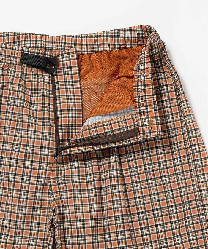 Close-up view of brick check colored Gramicci Checkered Shell Shorts on a light-tone background.