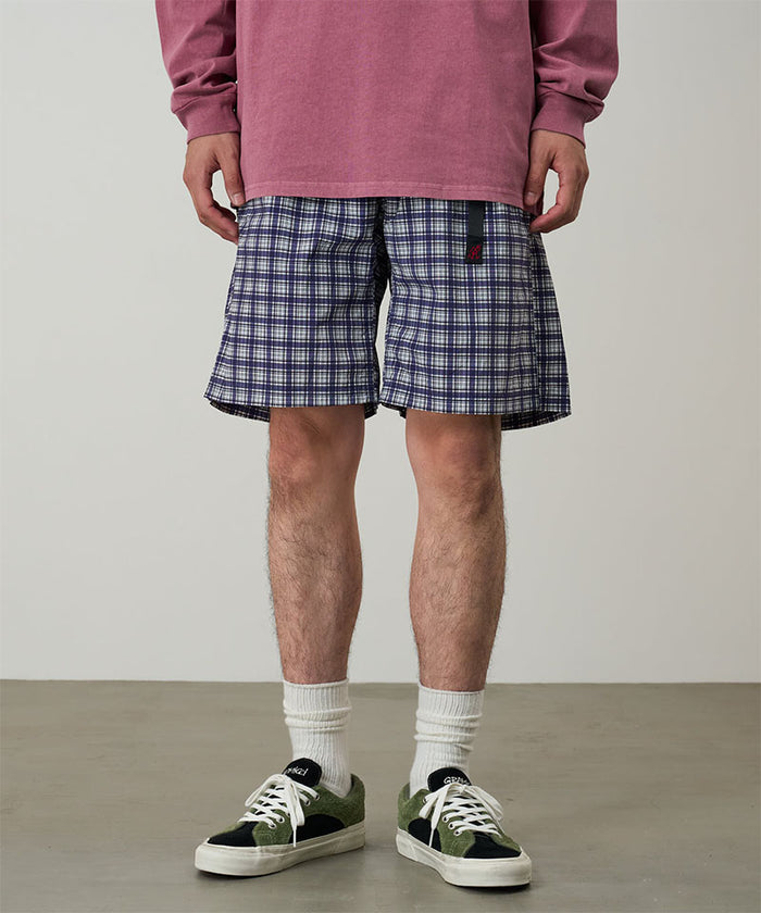 Model wearing navy check colored Gramicci Checkered Shell Shorts and a red shirt on a light-tone background.