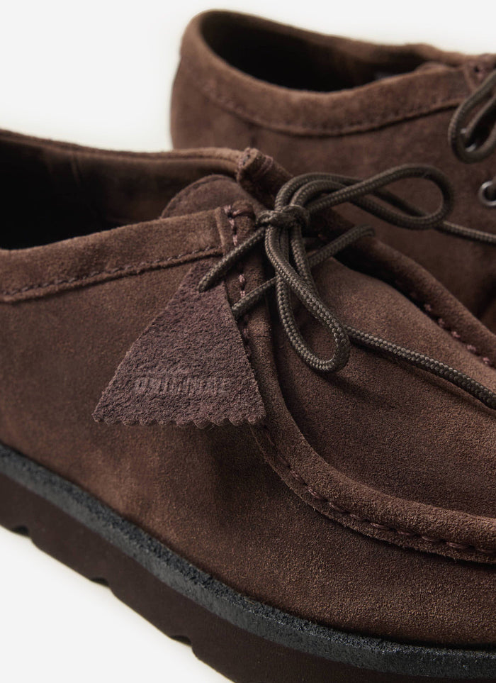 A close-up of the Clarks Originals Meare Walla shoes in dark brown suede from Percival, showing the lace-up and iconic tag.