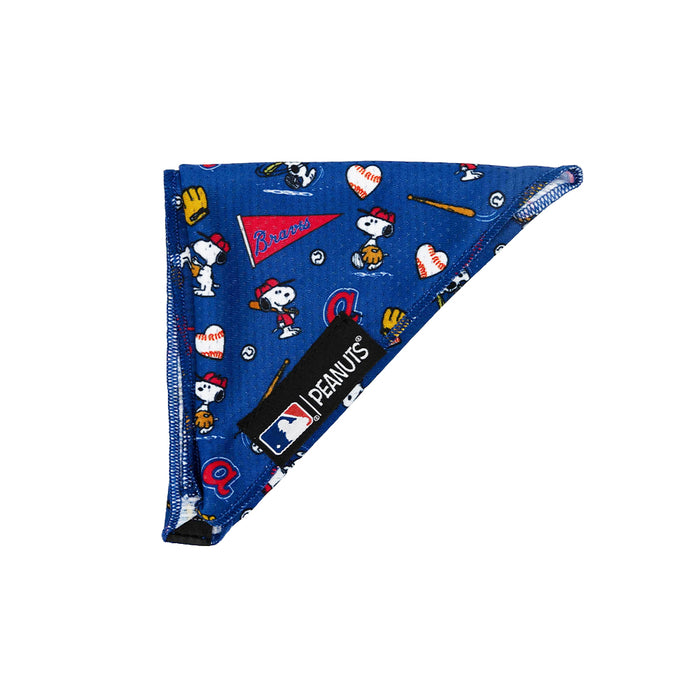 The Sassy Woof Dog Bandana - MLB™ x Peanuts™ Atlanta Braves™ is a blue triangular bandana with Snoopy, baseball gear, and a black tag featuring the Peanuts and MLB Atlanta Braves logos on the front.