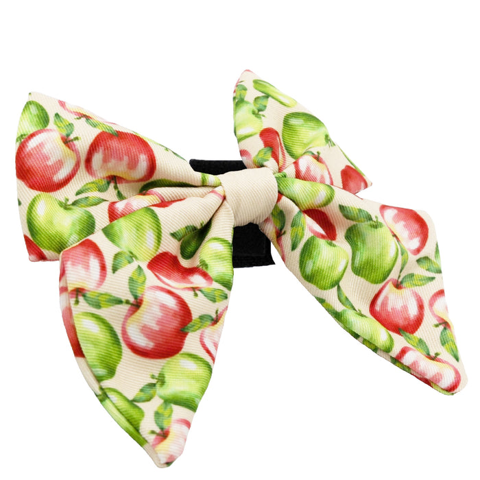 The Sassy Woof Dog Sailor Bow - Apple of My Eye features red and green apples on cream fabric, attached to a black elastic band—ideal for stylish pet accessories or adding flair to any dog harness.