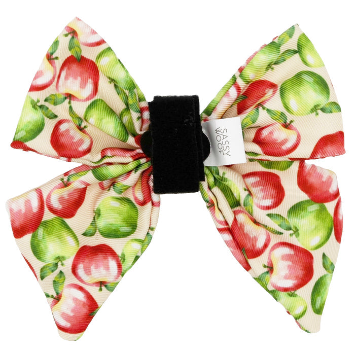 The Sassy Woof Dog Sailor Bow - Apple of My Eye features a playful red and green apple pattern on cream with a black center and a white tag accent, making it the perfect modern accessory for any dog harness.