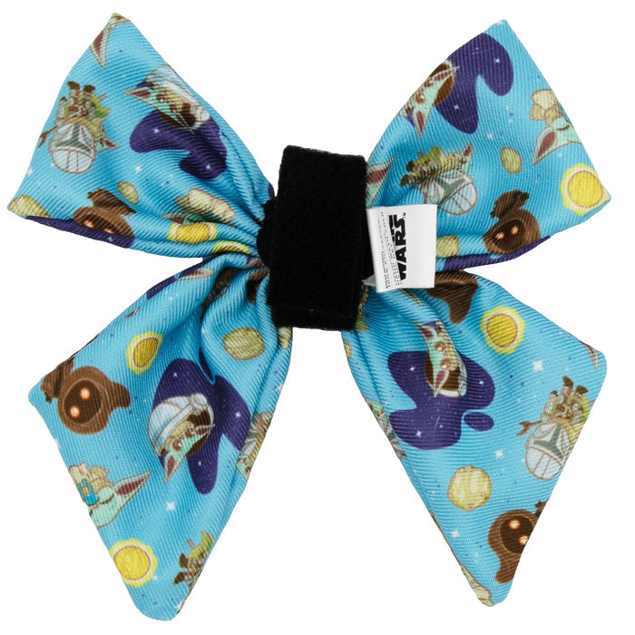 The Sassy Woof Dog Sailor Bow - STAR WARS™ The Mandalorian™ features blue fabric with Grogu, spaceships, and coins. It attaches to any adjustable harness via Velcro and includes a black band plus a white Star Wars logo tag.