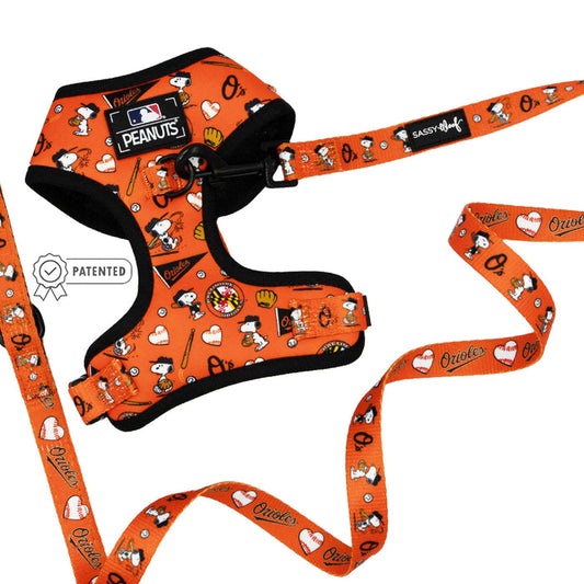 The Sassy Woof Dog Two Piece Bundle - MLB™ x Peanuts™ Baltimore Orioles™ includes an orange harness and leash with Snoopy, hearts, baseballs, team graphics, a Patented badge, MLB logo, and Sassy Woof label.