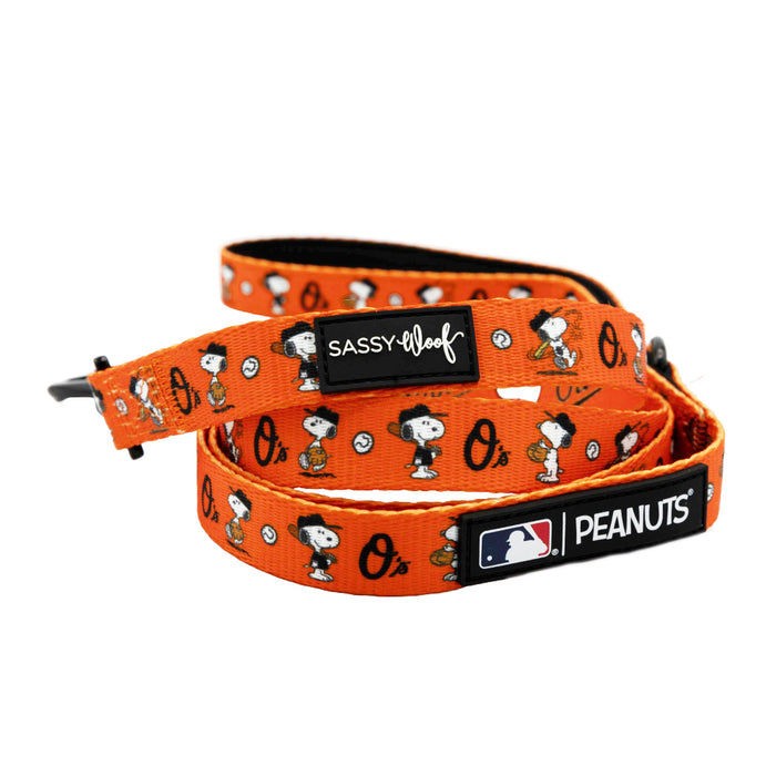 The Sassy Woof Dog Leash - MLB™ x Peanuts™ Baltimore Orioles™ is orange with Snoopy, Woodstock, and black “Sassy Woof” and “MLB Peanuts” labels.