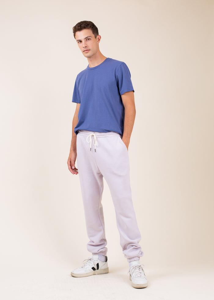 Man wearing a blue t-shirt and light purple sweatpants  on a beige background