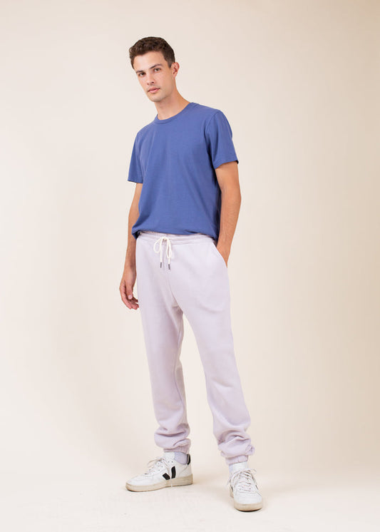 Man wearing a blue t-shirt and light purple sweatpants  on a beige background