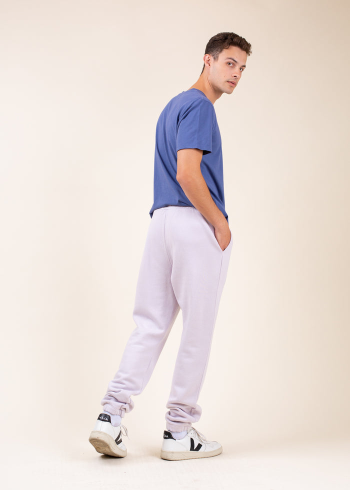 Man wearing a blue t-shirt and light purple sweat pants, from behind, against a beige background