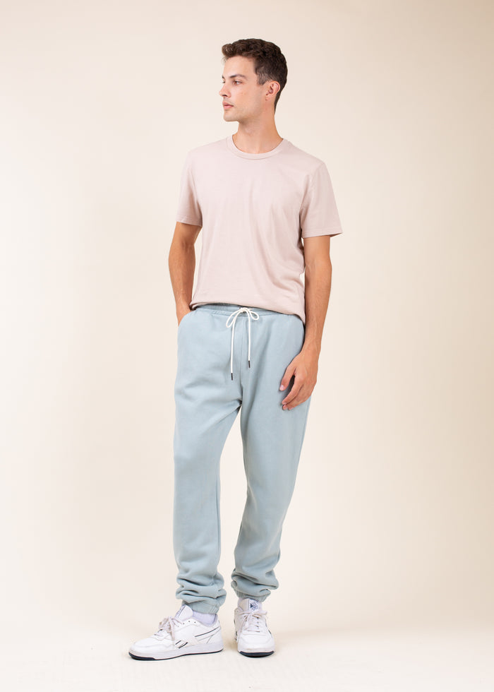 Man wearing a beige t-shirt and light blue sweatpants on a plain background