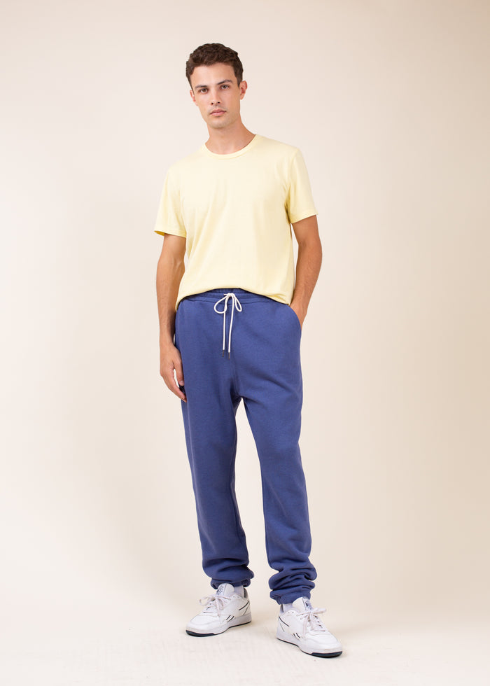 Man wearing a yellow t-shirt and dark blue sweatpants on a beige background