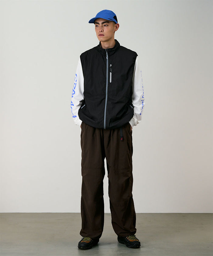 Model wearing a black Gramicci Flyweight Vest and brown pants on a light-tone background.