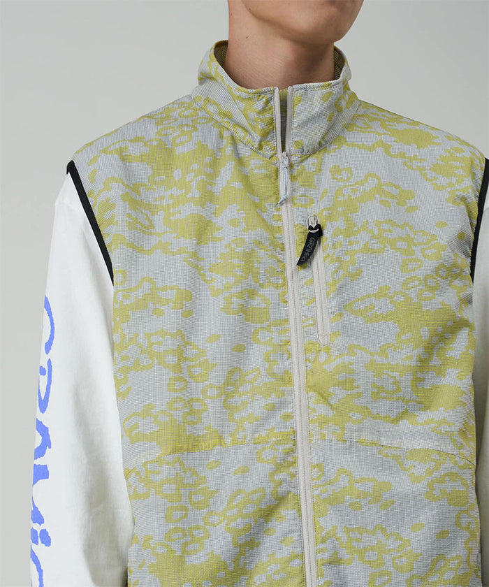 Model wearing a Gramicci yellow and grey grid camo Flyweight Vest against a light-tone background.