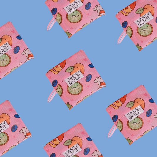 Sassy Woof Fruity Reusable Bags with orange, kiwi, strawberry, and blueberry prints are arranged in a repeating pattern on a solid light blue background.