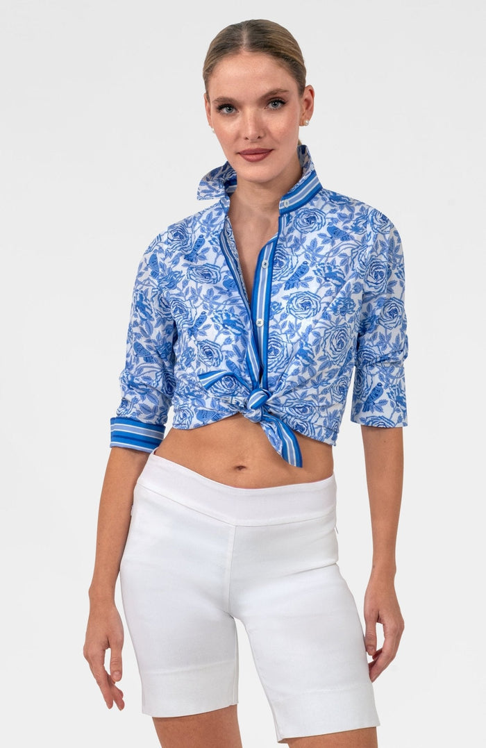 Woman wearing a blue and white patterned shirt with blue trim with white pants on white background