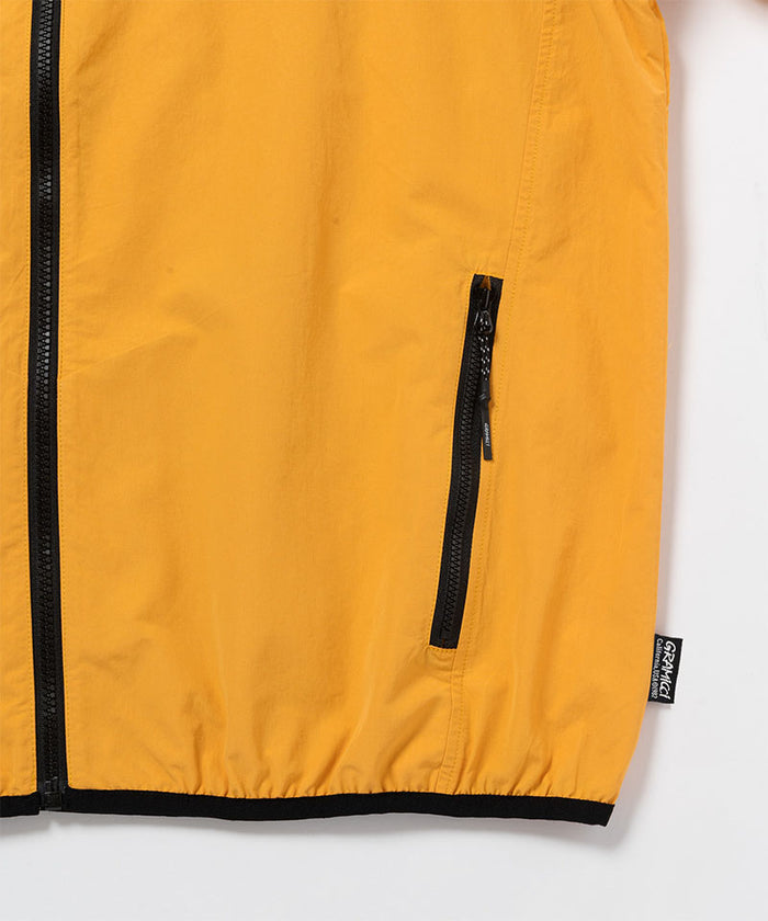 Close-up view of a Gramicci Gramicci Guide Jacket pocket in mango colored on a light-tone background.