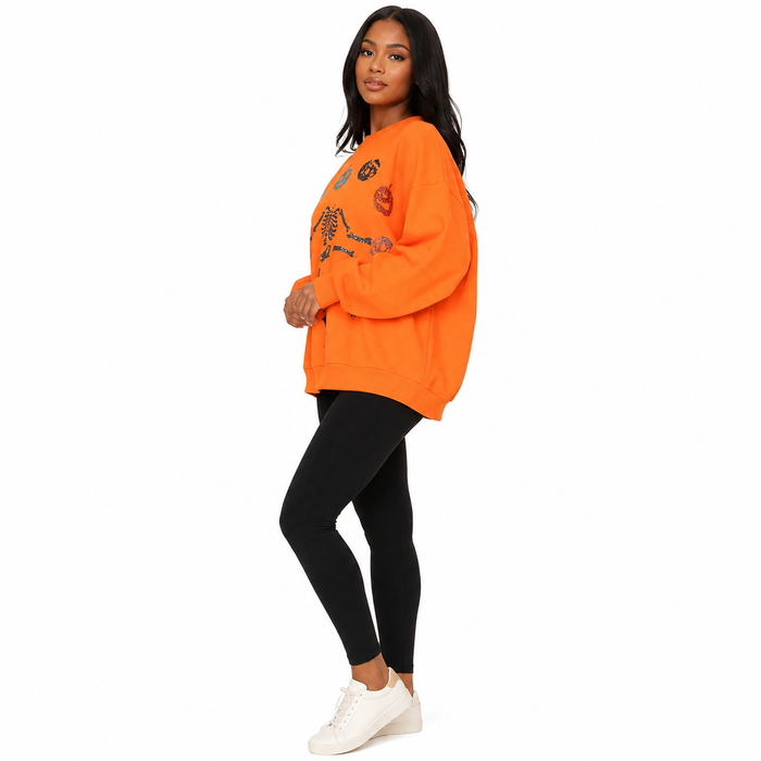 Side view of orange women's Halloween sweatshirt with long sleeves and skeleton pumpkin sequin detail on clean white backdrop