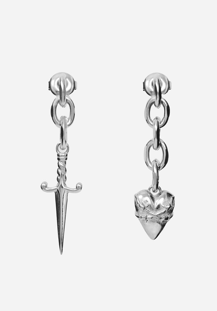 A pair of silver dangle earrings on a light gray background. One earring features a dangling dagger charm, and the other features a dangling spiked heart charm.