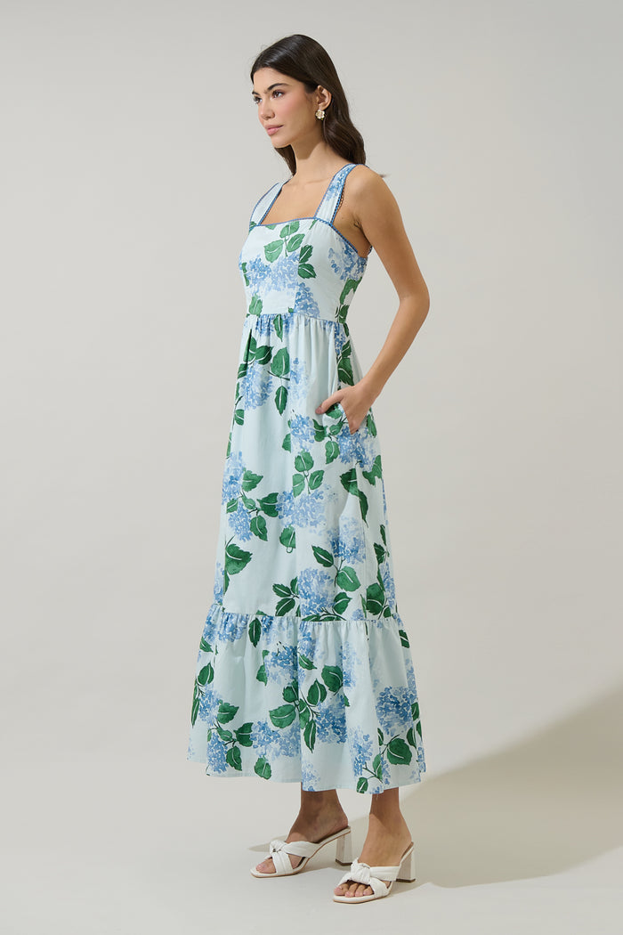 Woman wearing a long blue and green floral dress with hydrangeas with a white background