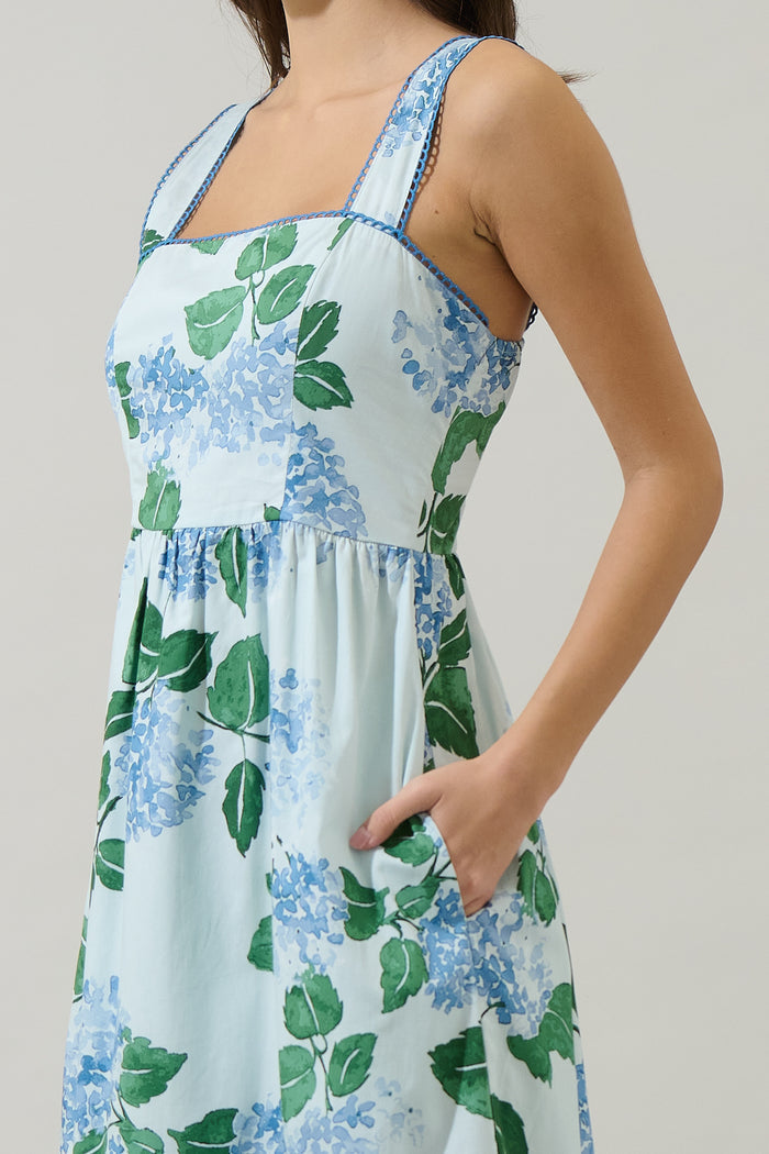 Woman wearing a long blue and green floral dress with hydrangeas with a white background