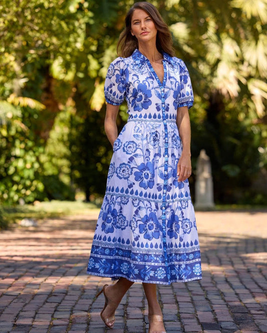 Woman wearing a long blue and white floral dress standing outdoors on a brick path
