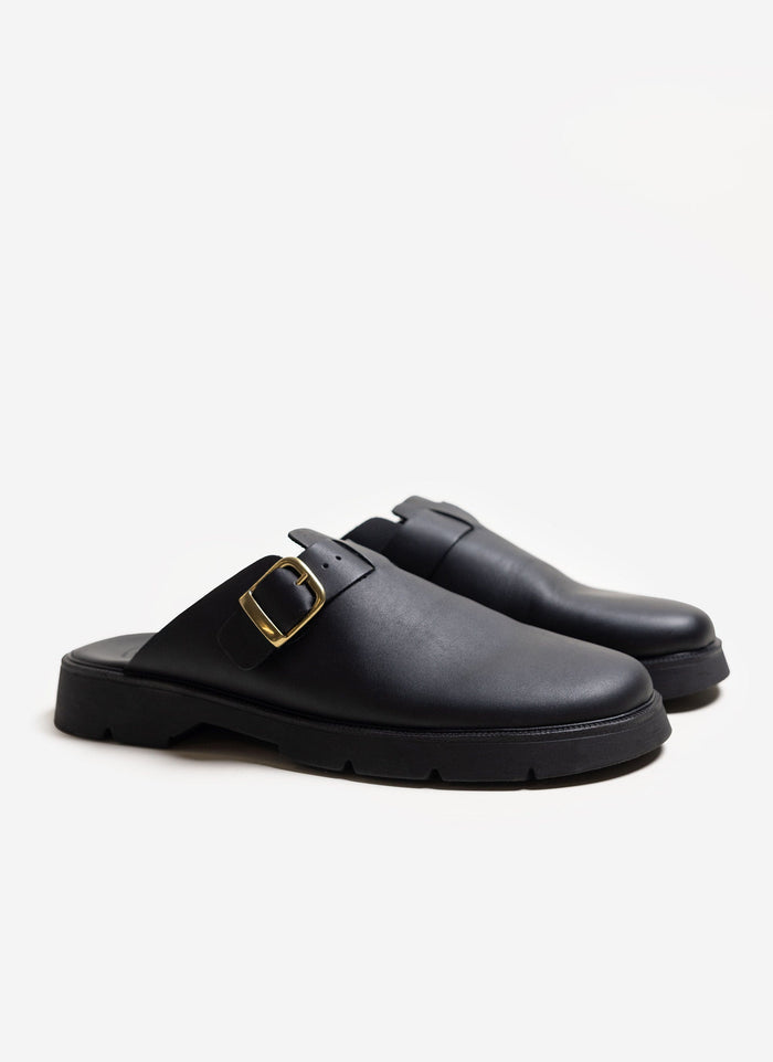 A pair of black leather Kleman Pacha sandals with a chunky sole and gold buckle, shot on a white background for Percival.
