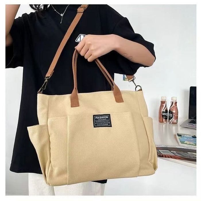 Women's canvas shoulder bag with horizontal shape, top handles and adjustable strap displayed for work, class and travel use.