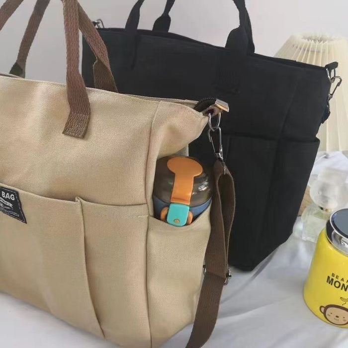 Canvas shoulder bag, with adjustable crossbody strap, top handles and front pocket shown for flexible daily carrying options.