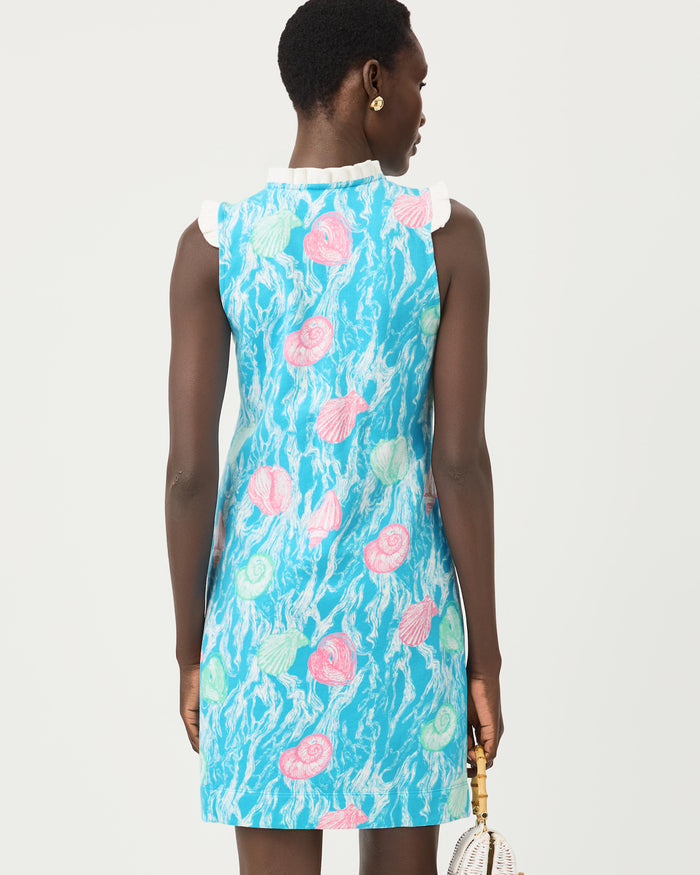 Woman wearing a blue dress with teal and pink seashell details, gold buttons, and white lace on a white background