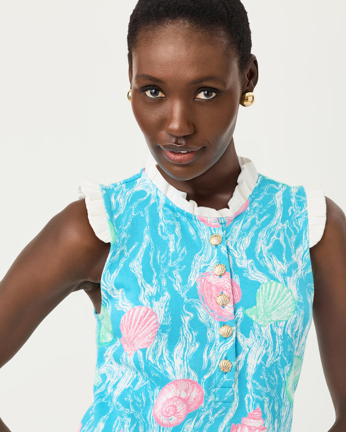 Woman wearing a blue dress with teal and pink seashell details, gold buttons, and white lace on a white background