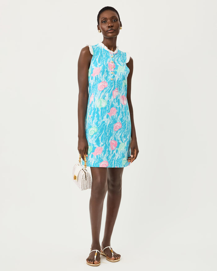 Woman wearing a blue dress with teal and pink seashell details, gold buttons, and white lace on a white background